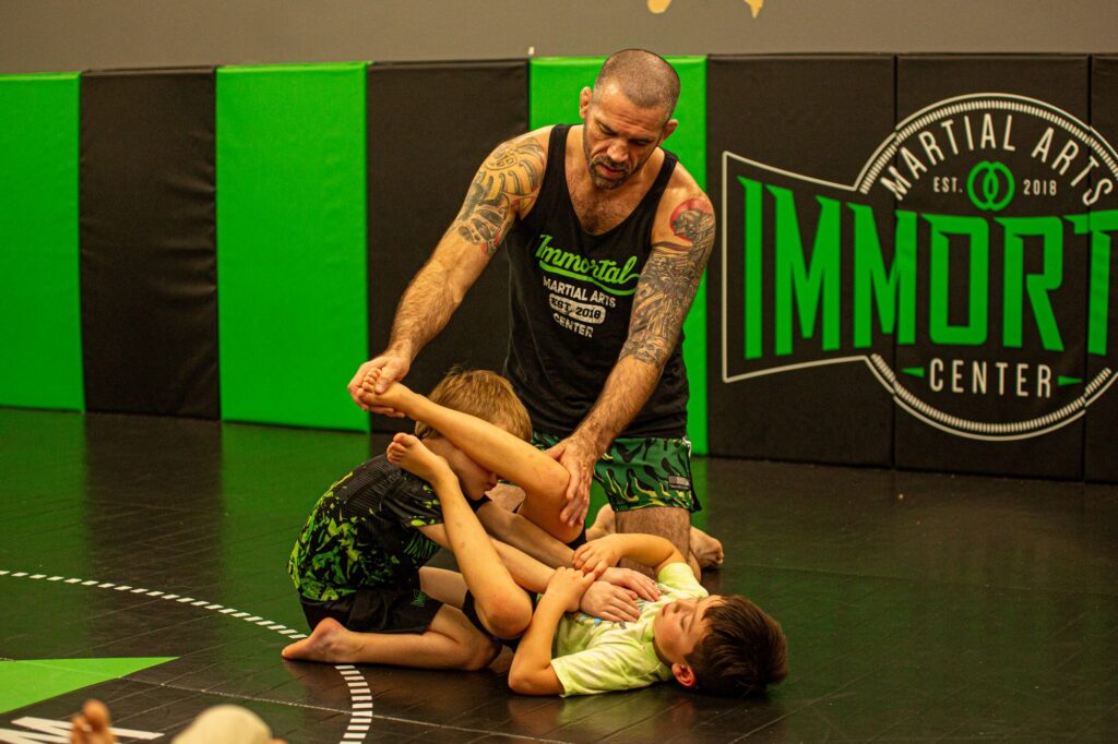 Coach demonstrating a jiu-jitsu technique with two kids on the mat